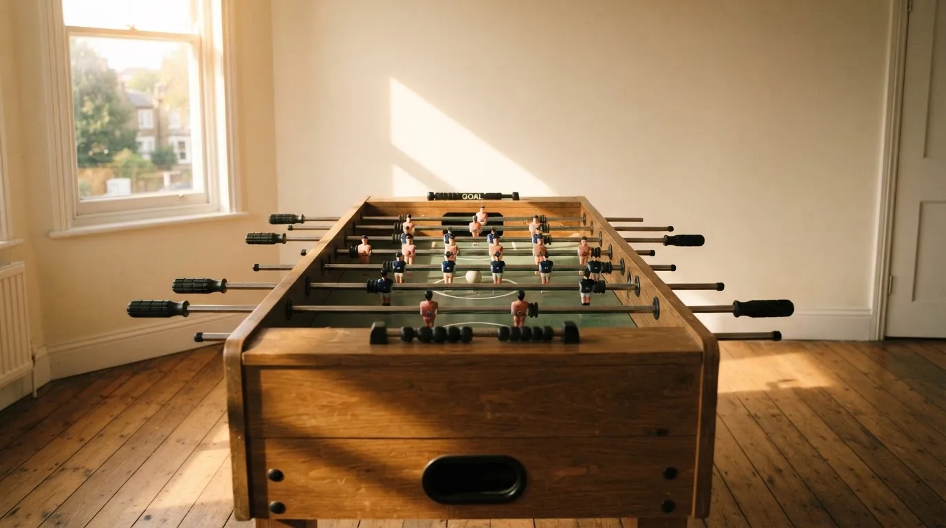 Ein Tischfussballtisch steht in einem leeren Aufenthaltsraum, Nachmittagslicht fällt durch ein Fenster.