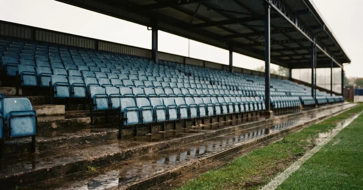 Eine Reihe leerer Sitzschalen auf der Tribüne eines kleinen Stadions, auf den Stufen glänzt Regenwasser.