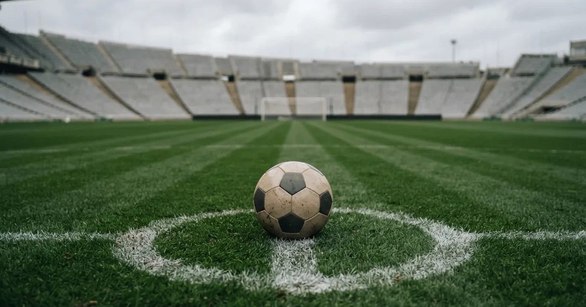 Ein Fussball liegt auf dem Anstosspunkt eines frisch gemähten Rasens, dahinter eine grosse Tribüne unter bewölktem Himmel